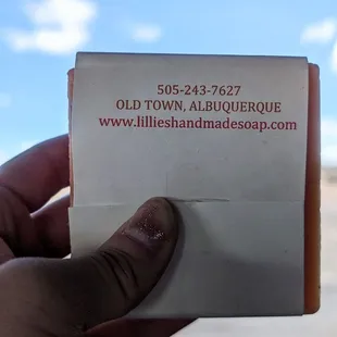 The back of Lillie&apos;s Handmade Soaps&apos; bar soap, which bears the shop&apos;s contact info, ft. NM scenery &amp; cornflower sky in the background