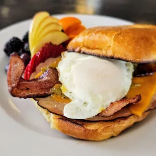 NM Bagel Sandwich with grilled ham, bacon, cheese, green chile, and a basted egg. Includes fruit