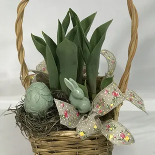 tulip blooming plant in a handled wicker basket decorated with ceramic bunny and over sized Easter egg, and spring ribbon