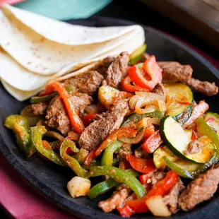 a plate of food with meat, vegetables, and tortillas