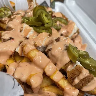 a tray of fries with sauce and jalapenos