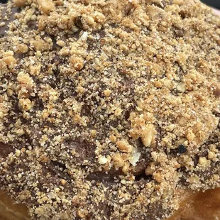 Cinnamon roll donut with chica Lee frosting topped with crushed peanuts.