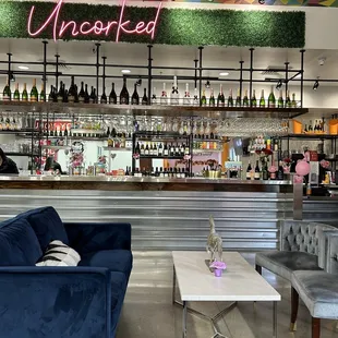 a bar with blue couches and a neon sign that reads uncorked