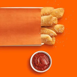 a bowl of ketchup and a bag of breadsticks