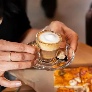 Hands holding small espresso glass with espresso and foam top