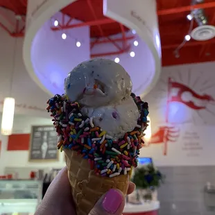 a hand holding an ice cream cone with sprinkles