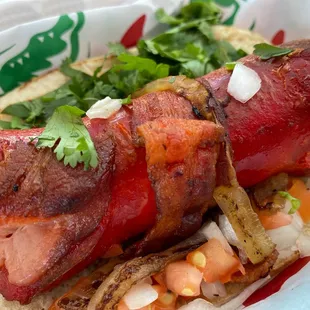 Mexican hot dog : bacon wrapped sausage topped with cilantro , grilled onions and diced tomatoes