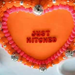 Orange and pink vintage-style wedding cake that says Just Hitched with disco balls for decoration