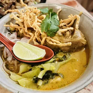 a bowl of soup with noodles and a lime wedge