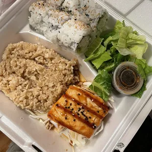 a takeout box with rice, salmon, lettuce, and salad