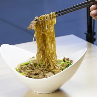 a person holding chopsticks over a bowl of noodles