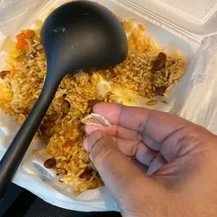 a hand holding a spoon over a container of rice