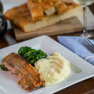 a plate of meat, mashed potatoes, and a glass of wine