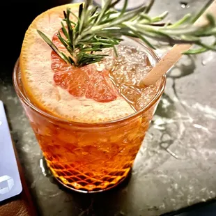 a glass of orange juice with a sprig of rosemary