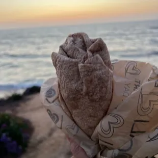 a person holding a pastry in front of the ocean