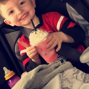 a young boy in a car seat holding a drink