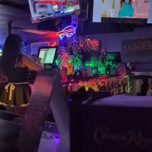  a woman sitting at a bar watching tvs