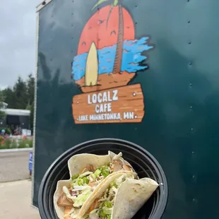 a hand holding a taco in front of a food truck