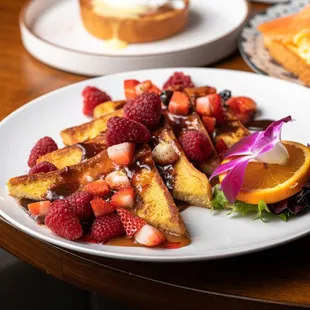 a plate of french toast with strawberries and orange slices