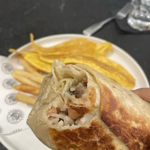 Lomorrito with carne asada. Background fries and fried plantain chips.
