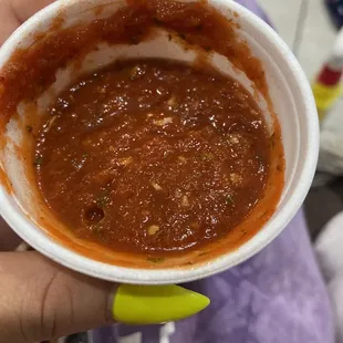 a hand holding a small bowl of sauce