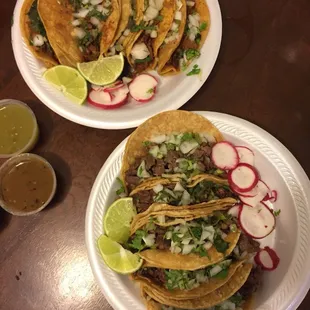 two plates of tacos with lime wedges and radishes
