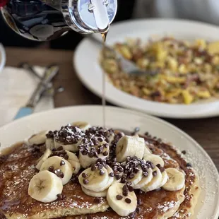 a person pouring syrup over a stack of pancakes