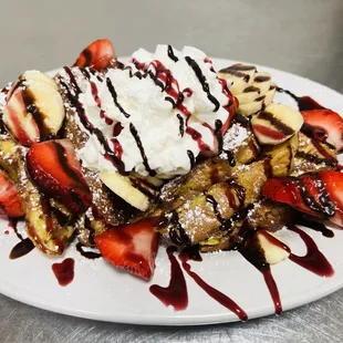 a plate of waffles with strawberries, bananas, and whipped cream