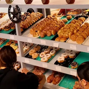 two women in front of a display of doughnuts