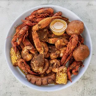 a bowl of crab legs, potatoes, corn, and corn on the cob
