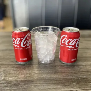 two cans of coke and a glass of ice
