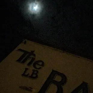 the moon in the sky above a bar sign