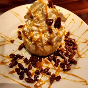 Cheesecake topped with whipped cream, caramel drizzles and candied pecans