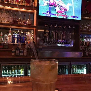 a drink on a bar with a television in the background