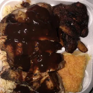 Rice, corn bread, plantains and jerk chicken with bbq sauce on top