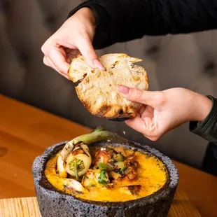 a person dipping a piece of bread into a bowl of soup