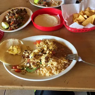 Scrambled eggs w/ bacon, beans, rice and tortillas, carne asada super taco to the left, small carnitas tacos in the middle.