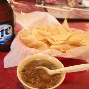 a bowl of salsa, chips, and a bottle of lite