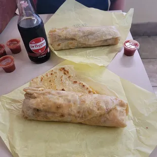 two burritos and a soda on a table