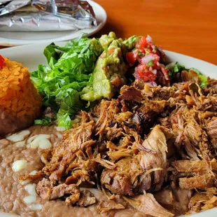 Carnitas with four flour tortillas, guacamole, salad, yellow rice and fried beans.