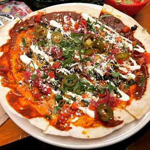 Tostada pizza-crispy jumbo flour tortilla, black beans, pickled veggies, chingon cheese, crema, scallion, cilantro