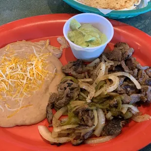 Beef fajitas with beans, guacamole, a green chile strip and sautéed onions.