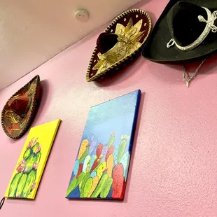 a pink wall with paintings and hats on it