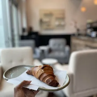 a person holding a plate with a croissant on it
