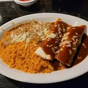 Two chicken burritos with enchilada sauce and melted cheese, rice and beans.