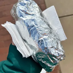 a person holding a sandwich wrapped in foil