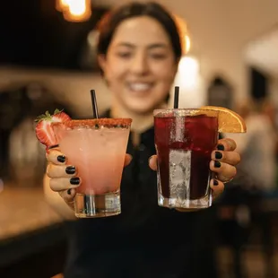 a woman holding two cocktails