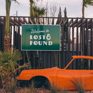 an orange car parked in front of a sign