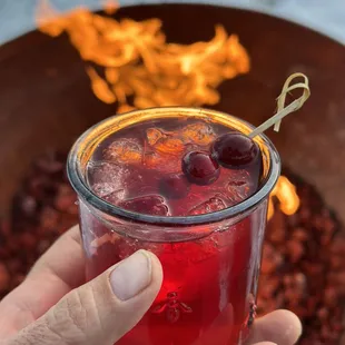 a person holding a drink in front of a fire