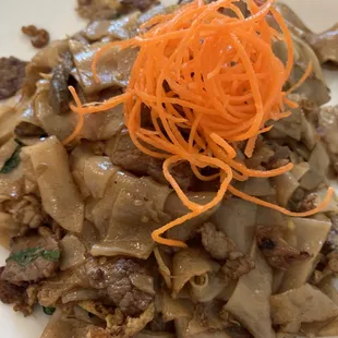 Pad Kee Mow: Smoky wide rice noodles with stir fried with all natural beef, onions, sweet basil, spicy Thai chili, garlic, and tomato.